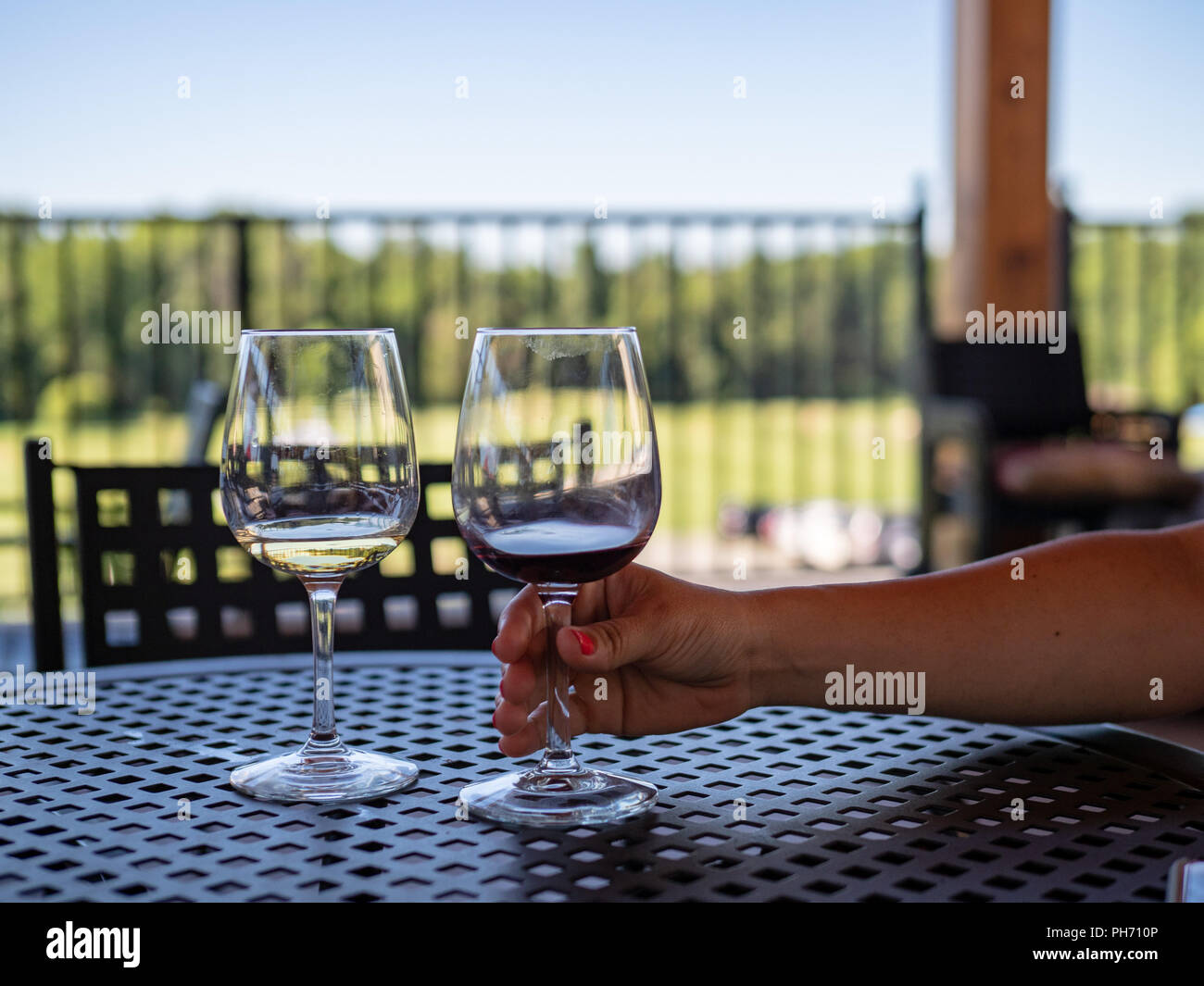 Bras de la femme pour atteindre presque vide verres de vin rouge et blanc sur un patio extérieur table Banque D'Images