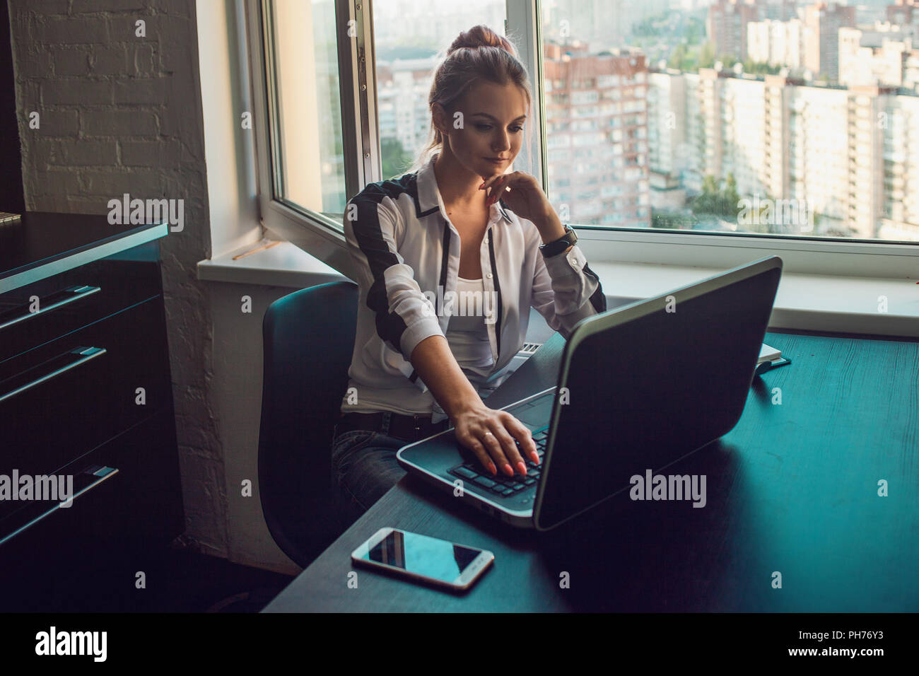 Jeune blonde travaille sur un ordinateur portable. Fille dans un bureau moderne, loft intérieur, code vestimentaire décontracté Banque D'Images