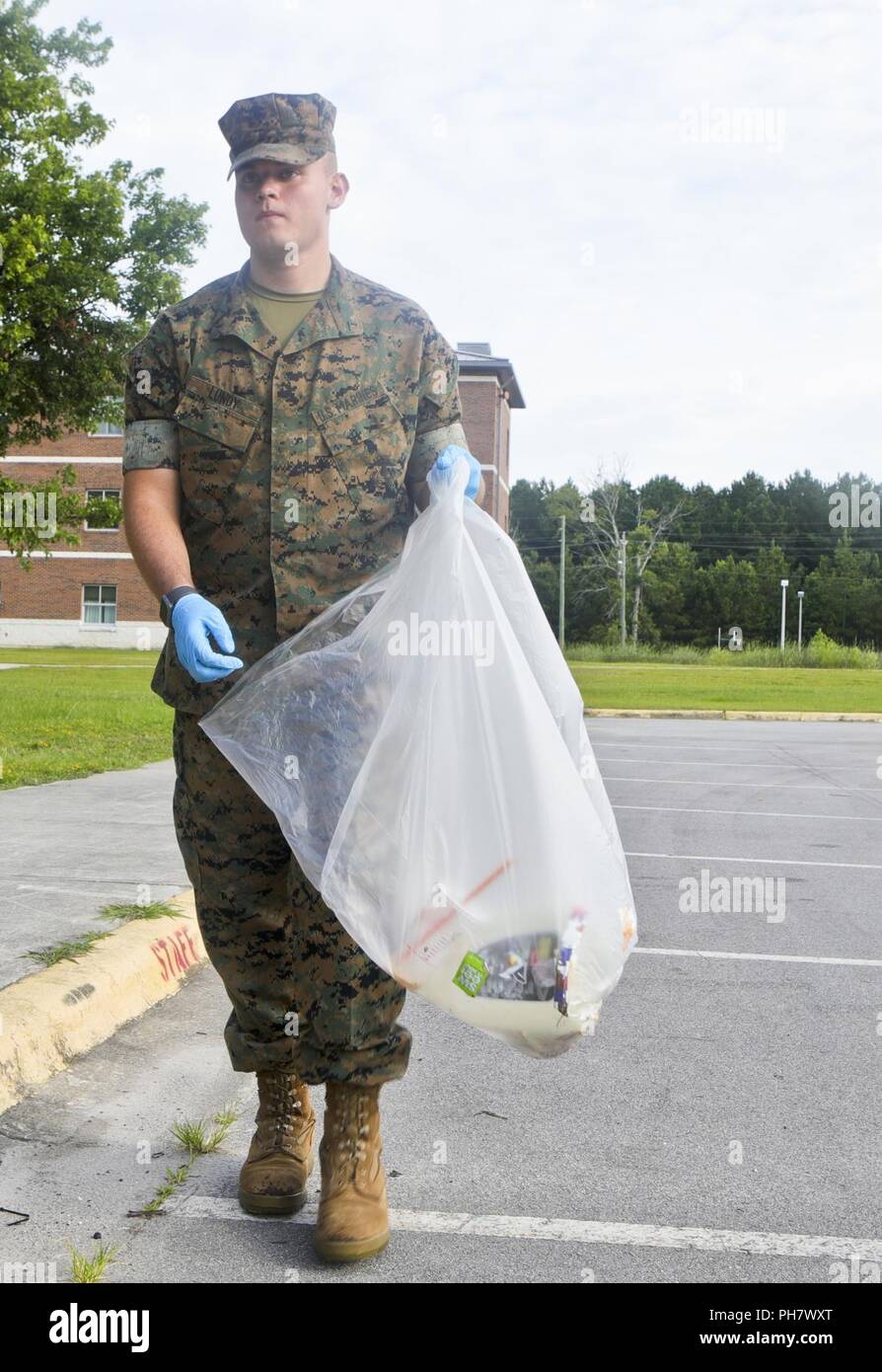 Circuit des Marines des États-Unis. Joshua Lundy, un greffier de l'administration des approvisionnements affectés au Siège et Service Company (H&S Co.), du Marine Corps Combat Service Support des écoles, se jette dans la corbeille trashbag lors d'une journée de nettoyage de la Terre au Camp Johnson, N.C., le 26 juin 2018. H&S Co. procède à une terre journée de nettoyage de la base pour promouvoir la sensibilisation à l'environnement. Banque D'Images