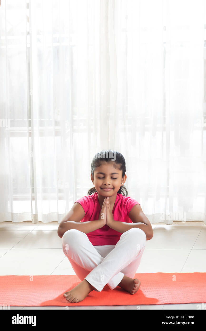 Petite fille faisant la prière sur un tapis de yoga à la maison Banque D'Images