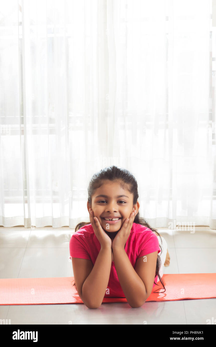 Little girl with hand on chin allongé sur un tapis de yoga Banque D'Images
