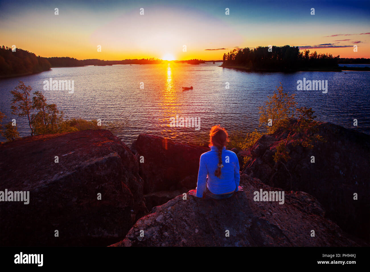 Femme assise sur le rocher et à la recherche au coucher du soleil Banque D'Images