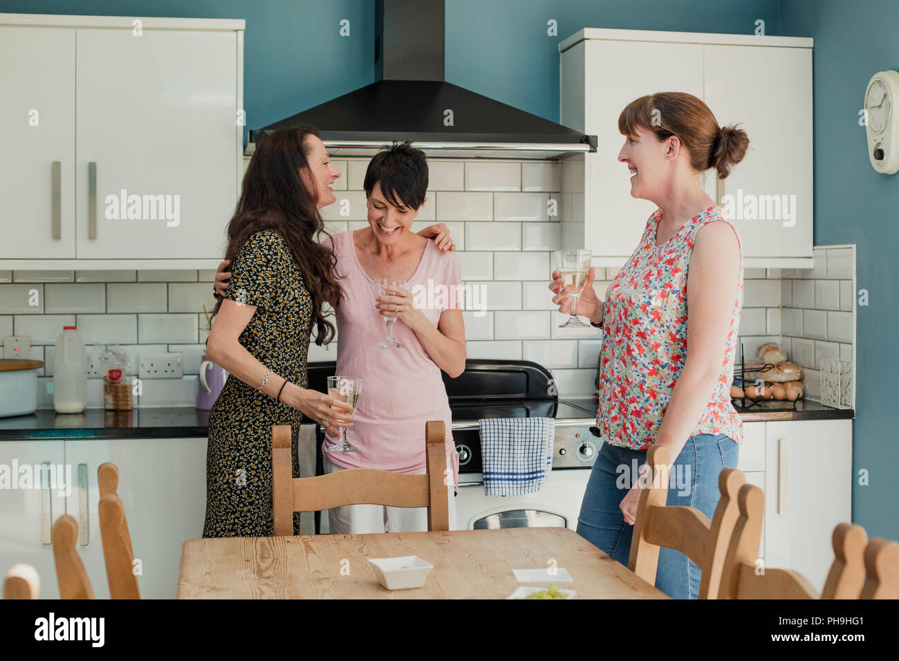 Trois femmes adultes possèdent debout dans un buvant un verre de vin. Les femmes sont tous debout autour du poêle dans la cuisine, parler et rire Banque D'Images