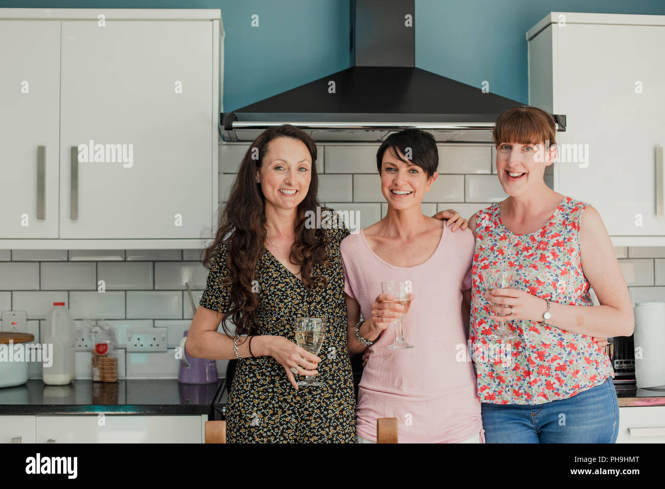 Trois femmes adultes possèdent debout dans un buvant un verre de vin. Les femmes sont tous debout autour du poêle dans la cuisine, à la recherche au camer Banque D'Images