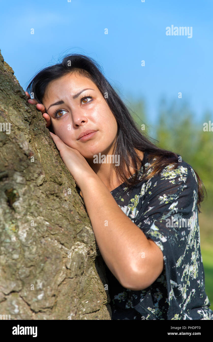 Young woman leaning against tree trunk Banque D'Images