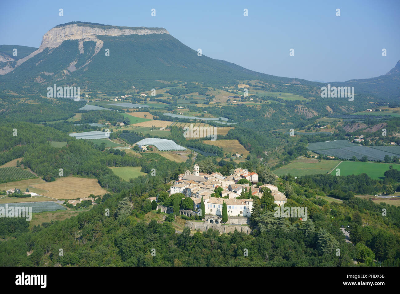 VUE AÉRIENNE. Village médiéval perché entouré de vergers, le Mont Saint-Genis au loin. Ventavon, Hautes-Alpes, Provence, France. Banque D'Images
