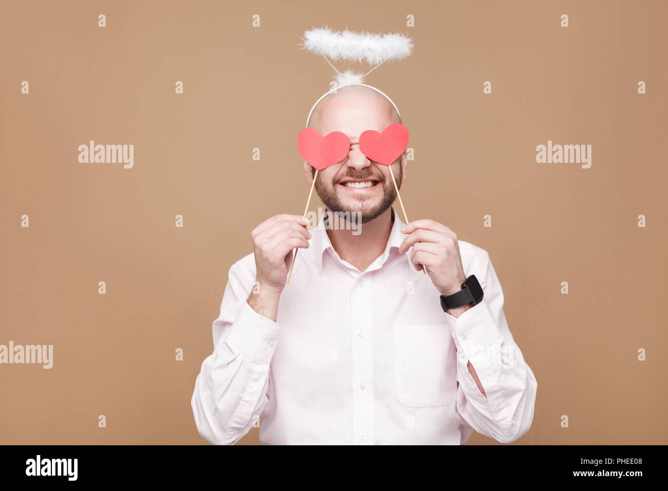 Heureux âge moyen beau barbu chauve en chemise blanche Ange debout, fermer les yeux avec deux autocollants coeur et halo sur la tête et sourit à pleines dents. studi Banque D'Images Heureux âge moyen beau barbu chauve en chemise blanche Ange debout, fermer les yeux avec deux autocollants coeur et halo sur la tête et sourit à pleines dents. studi Banque D'Images