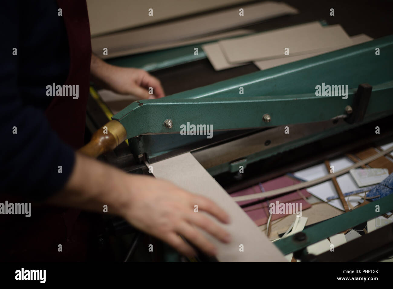 Coupe homme et du papier sur une grande carte guillotine sur une table de travail dans un atelier relieurs dans une vue en gros plan Banque D'Images