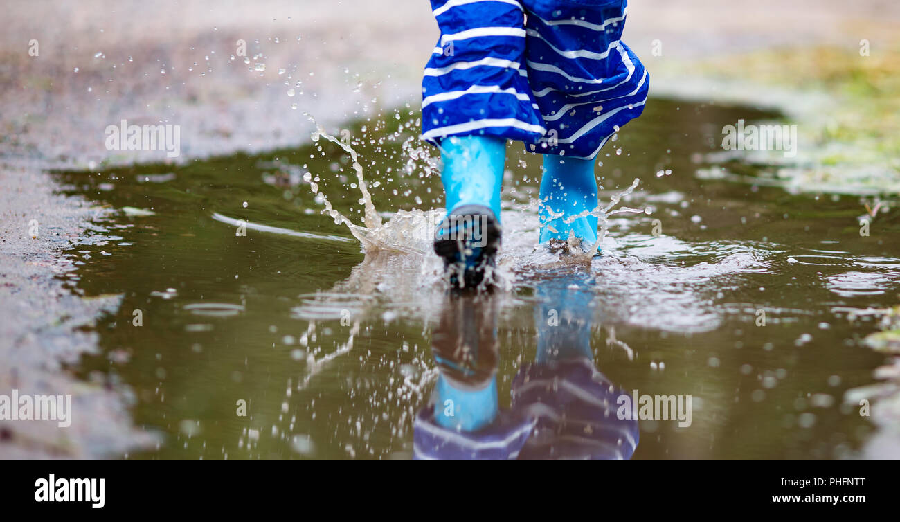 La marche de l'enfant dans la flaque en wellies sur temps de pluie Banque D'Images