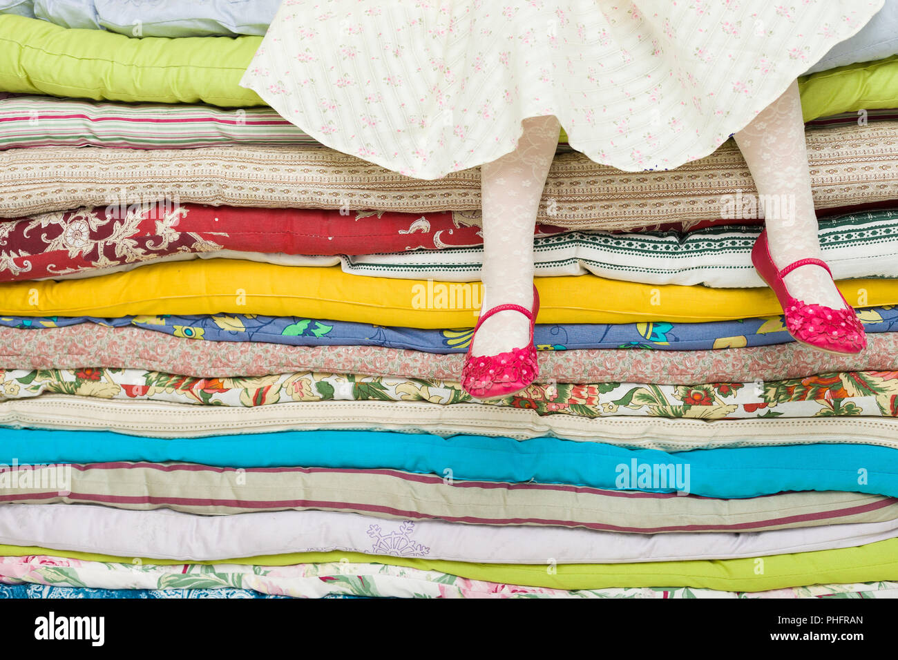 Les jambes d'une petite fille assise sur une pile de matelas colorés. Décorations pour le conte de fées La princesse sur un petit pois Banque D'Images