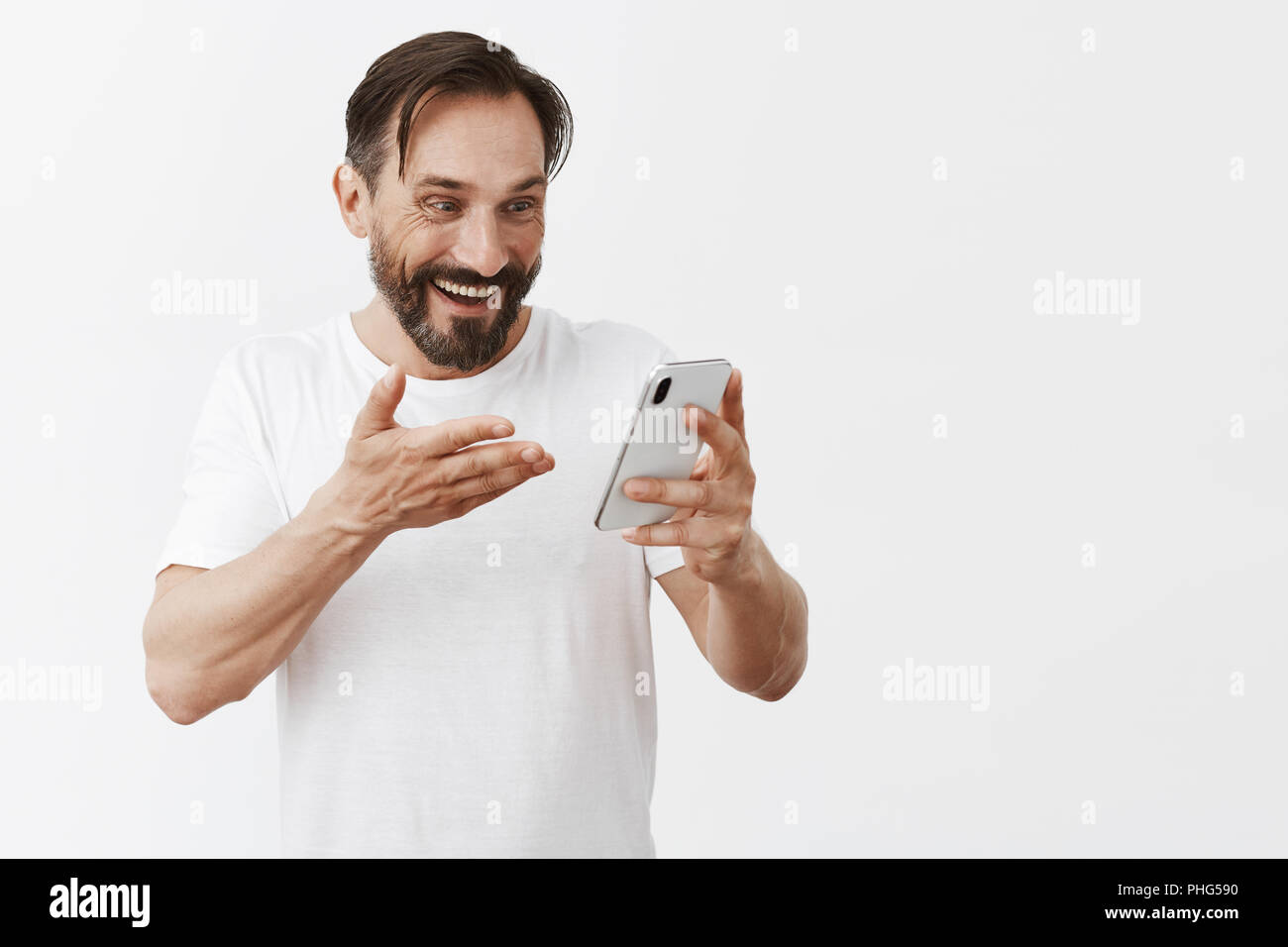 S'il n'est miracle. Surpris et heureux de l'homme surpris en t-shirt blanc, holding smartphone et en montrant l'écran du périphérique avec satisfait et excité, expression étonné avec chèque Banque D'Images