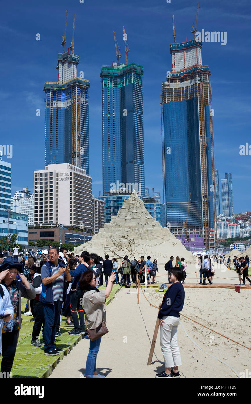 2018 Festival de sable de Haeundae, Busan, Corée. La foule sur la plage en face de la sculture de hautes tours modernes en construction derrière Banque D'Images