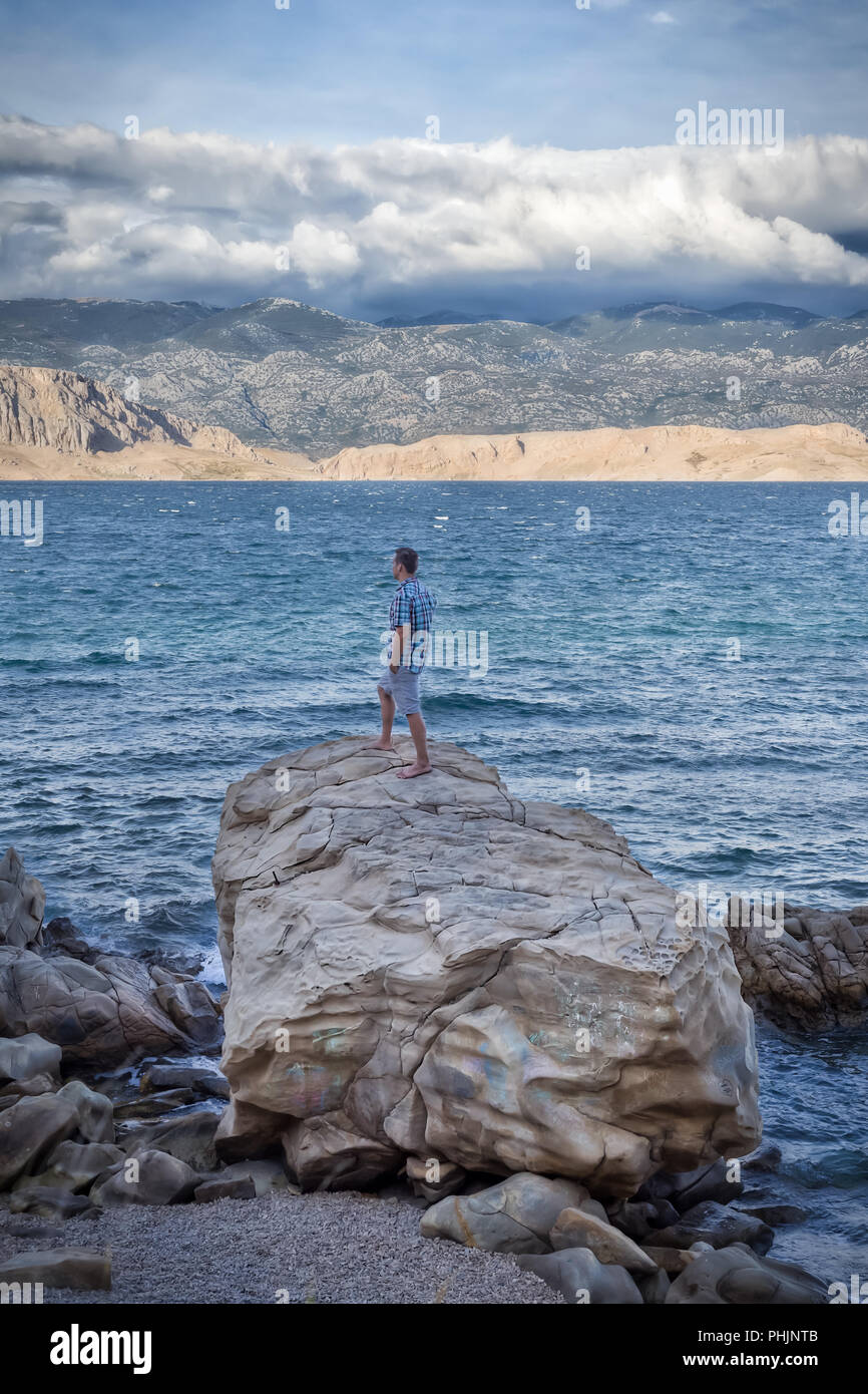 Homme debout sur un gros rocher sur une plage de l'île de Pag, Croatie. Banque D'Images