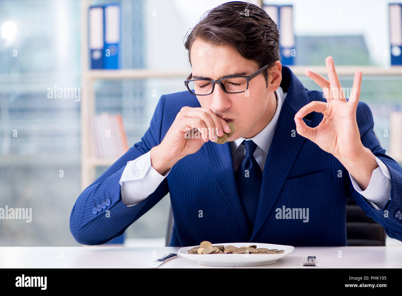 Funny businessman eating des pièces d'or in office Banque D'Images