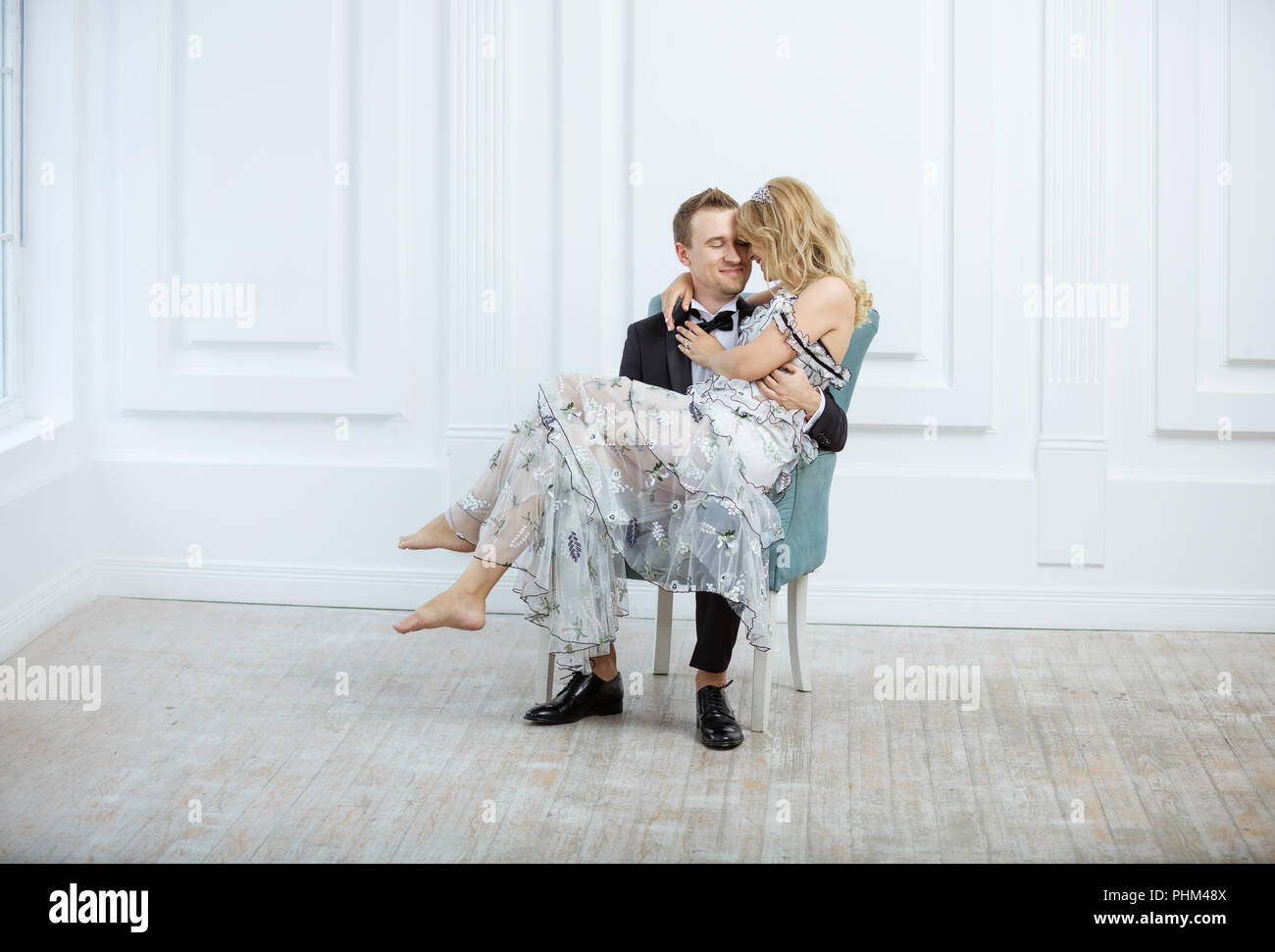 Jeune couple dans le quartier à la mode de vêtements de luxe s'embrasser et de rire tout en restant assis dans un fauteuil à l'intérieur Banque D'Images