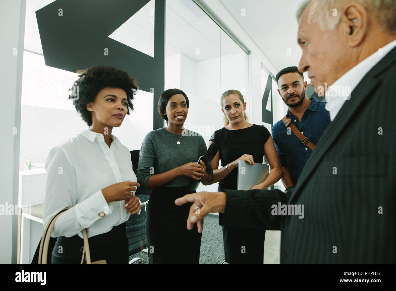 Les jeunes de l'équipe d'entreprise à l'écoute pour conseiller la haute direction du bureau en couloir. Groupe d'affaires talking in office corridor. Banque D'Images