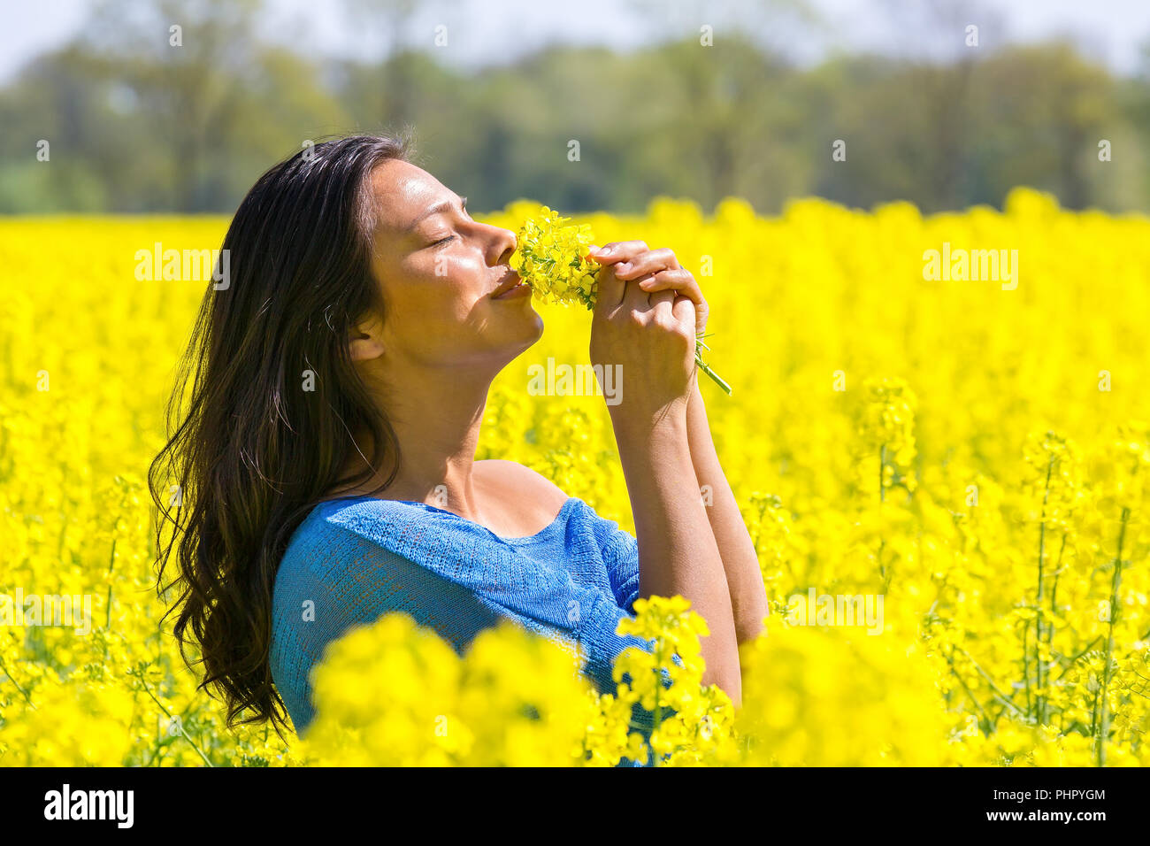 Woman smelling flowers in yellow rapeseed field Banque D'Images