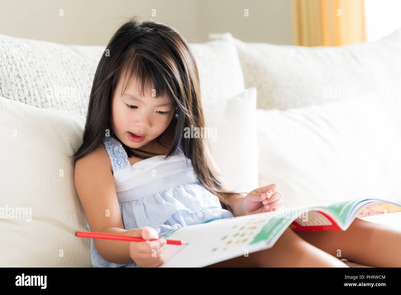 Happy cute little girl smiling and holding red crayon et le dessin, l'écriture sur un livre pour faire ses devoirs. kid concept de l'éducation. Banque D'Images