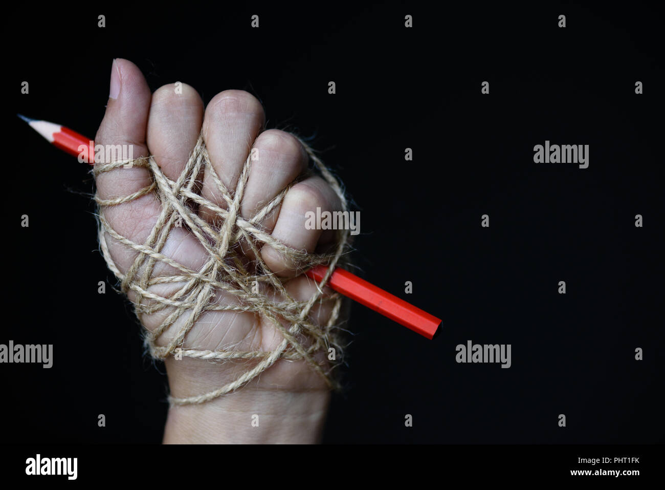 La main avec crayon rouge attaché avec de la corde, illustrant l'idée de la liberté de la presse ou la liberté d'expression sur fond sombre en bas-clé. Les Banque D'Images