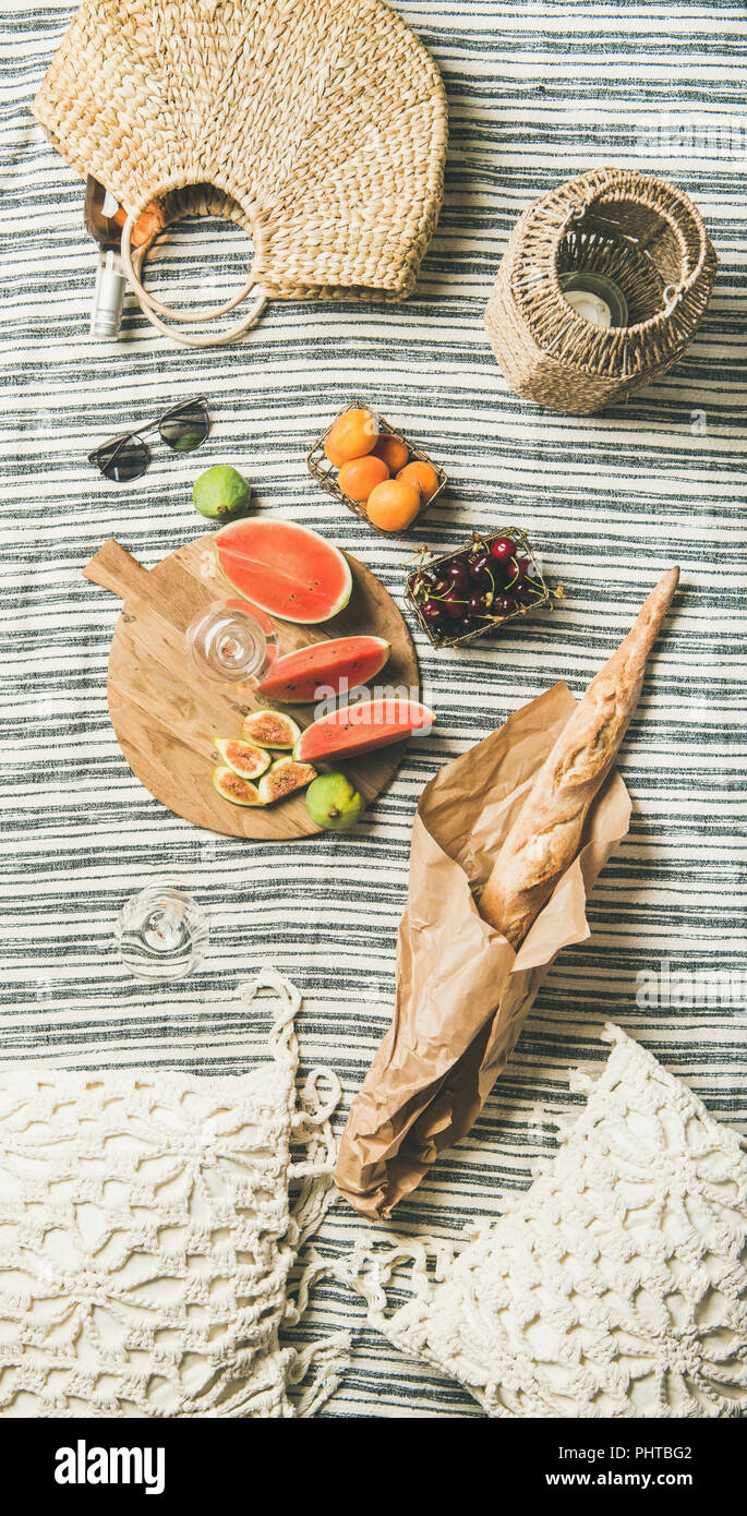 Pique-nique d'été. Vin rose en verre et la bouteille, fruits frais à bord, de la baguette sur la couverture et la femme Sac de paille, vue du dessus. Rassemblement en plein air ou Banque D'Images