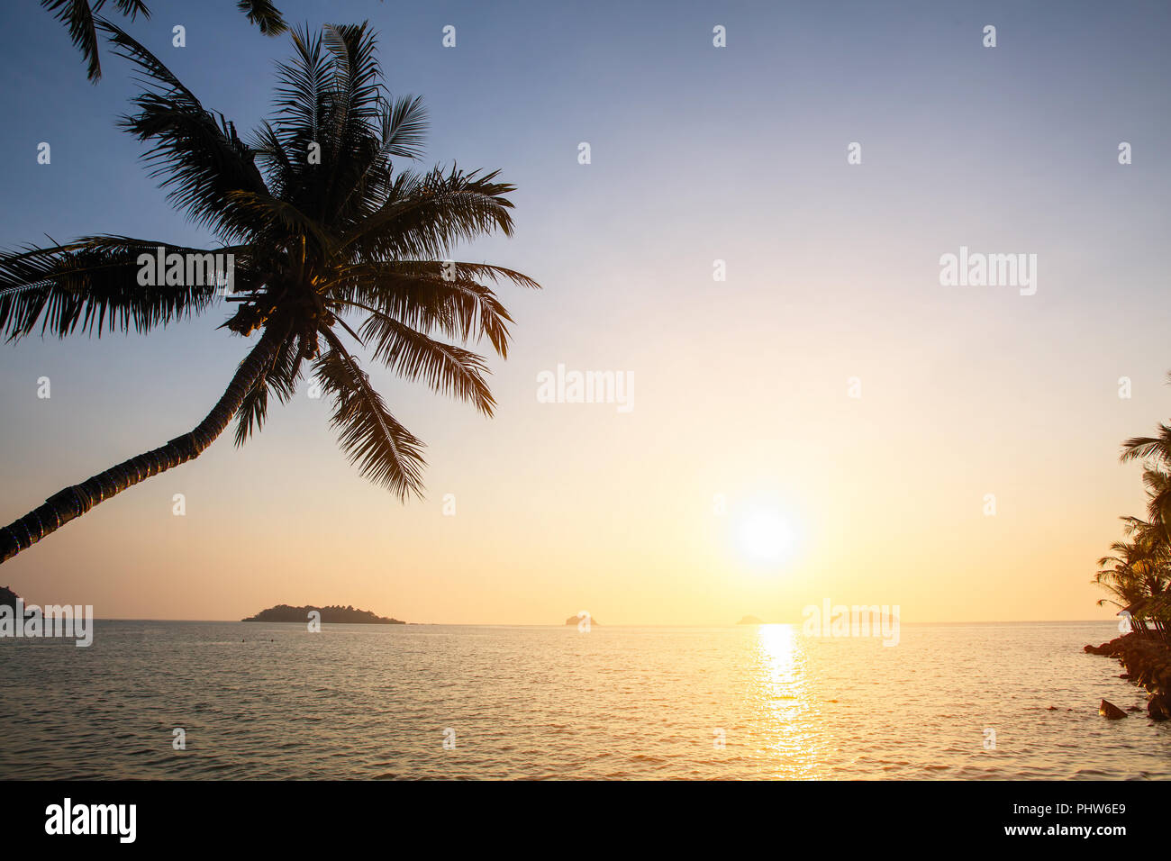 Coucher du soleil sur la côte tropicale avec des silhouettes de palmier au-dessus de l'eau. Banque D'Images
