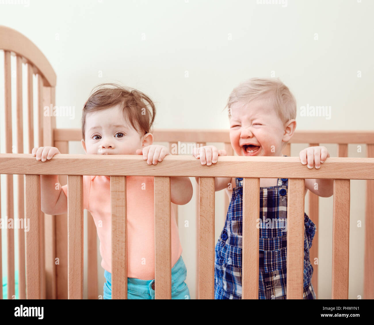 Portrait de deux adorables bébés mignon drôle frères et sœurs les amis de neuf mois au lit permanent lit-bébé suçant manger mâcher côtés en bois de pleurer, à la recherche dans Banque D'Images