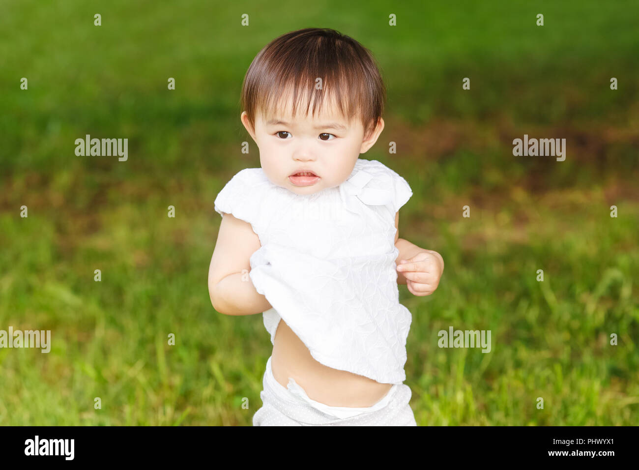 Portrait Of Cute Adorable Petite Fille Asiatique Enfants Bebe D Un An Dans Un Pantalon Blanc Shirt Debout Sur L Herbe De Prairie Sur Le Terrain De Jeu Sur Le Coucher Du Soleil Photo