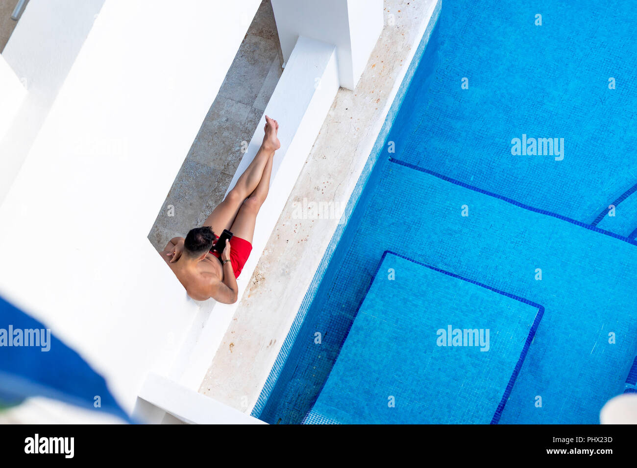 Capture d'Ariel un beau jeune homme athlétique et de détente près de la piscine ou à l'aide de SMS d'un téléphone cellulaire ou un téléphone mobile sur une maison de luxe Banque D'Images