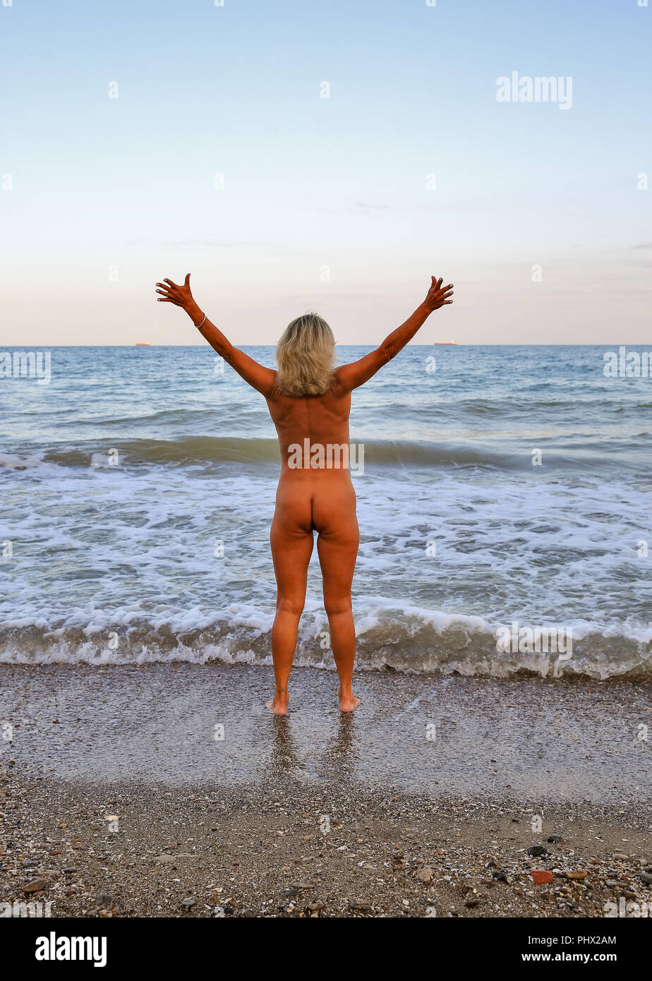 Belle femme nue se trouve avec son dos dans le sable sur la plage de la mer  au coucher du soleil Photo Stock - Alamy