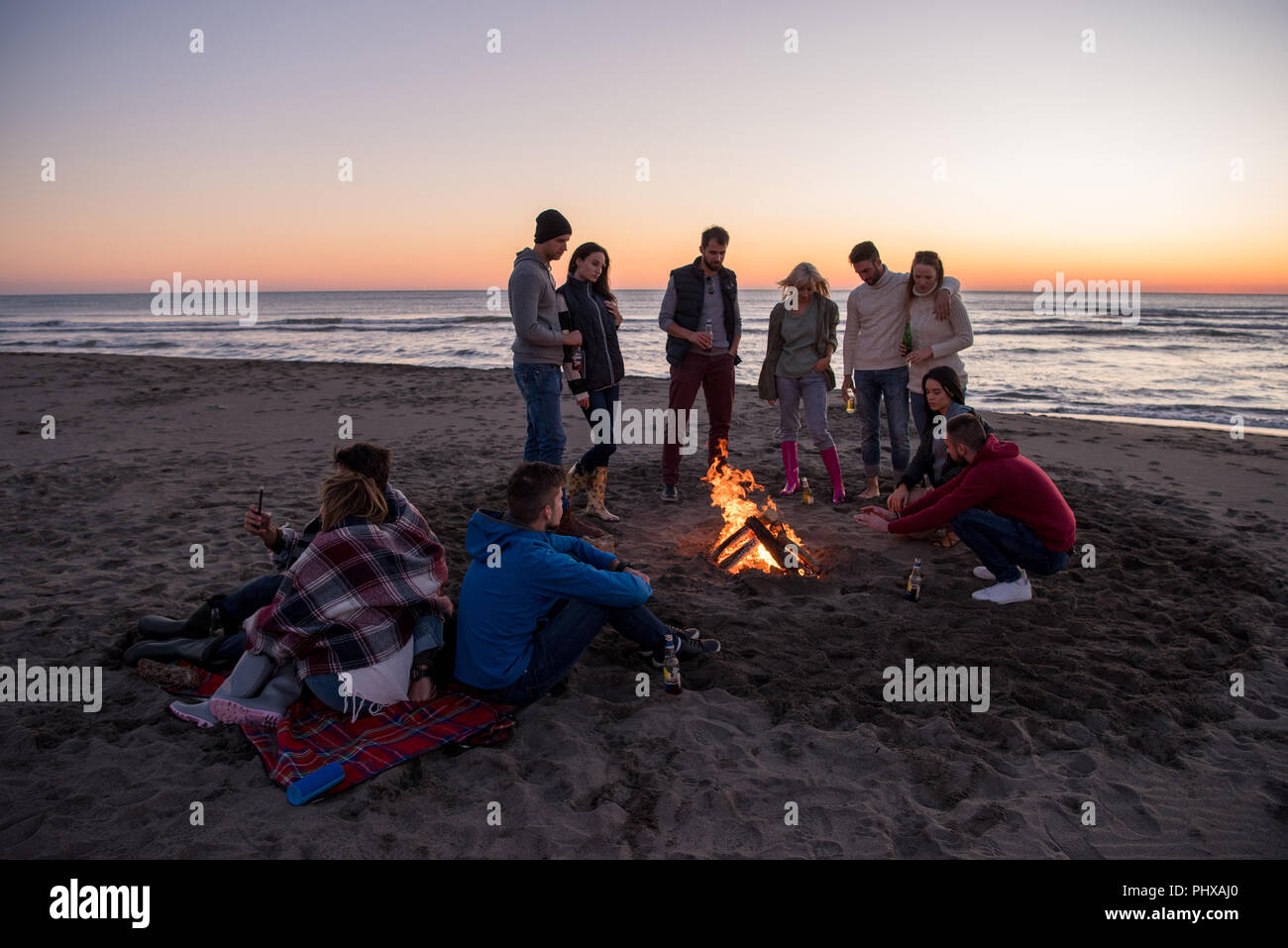 L'insouciance heureuse jeunes amis de s'amuser et de boire une bière par Bonefire sur la plage alors que le soleil commence à définir Banque D'Images