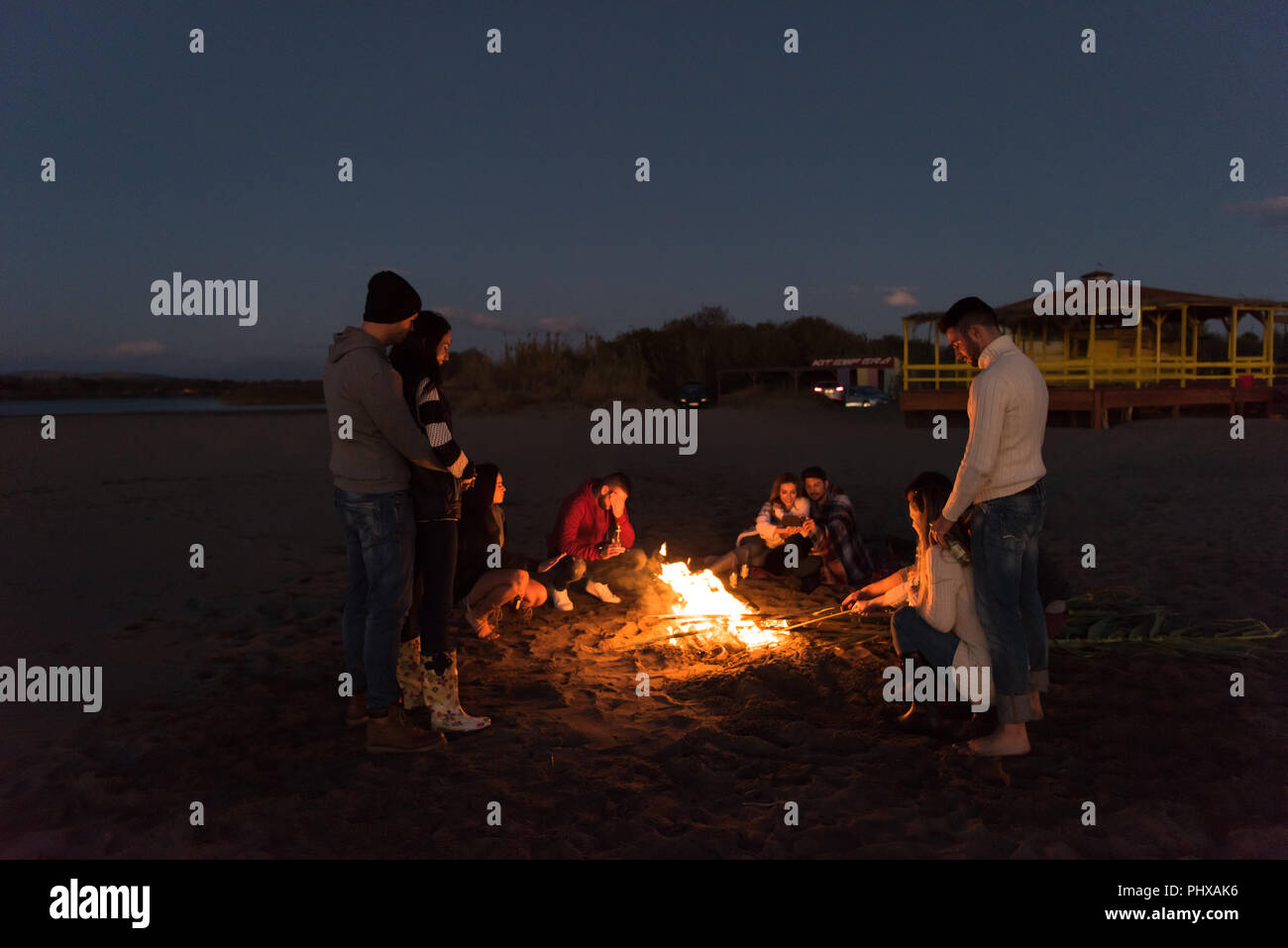 L'insouciance heureuse jeunes amis de s'amuser et de boire une bière par Bonefire sur la plage alors que le soleil commence à définir Banque D'Images
