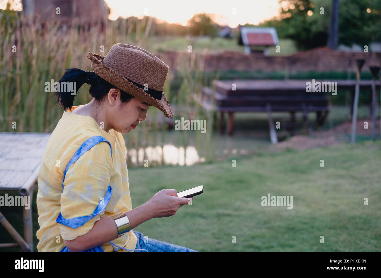 Femme Asiatique porter hat assis à l'extérieur utiliser mobile téléphone au jardin avec sentiment chill out.relax vie Loisirs Banque D'Images