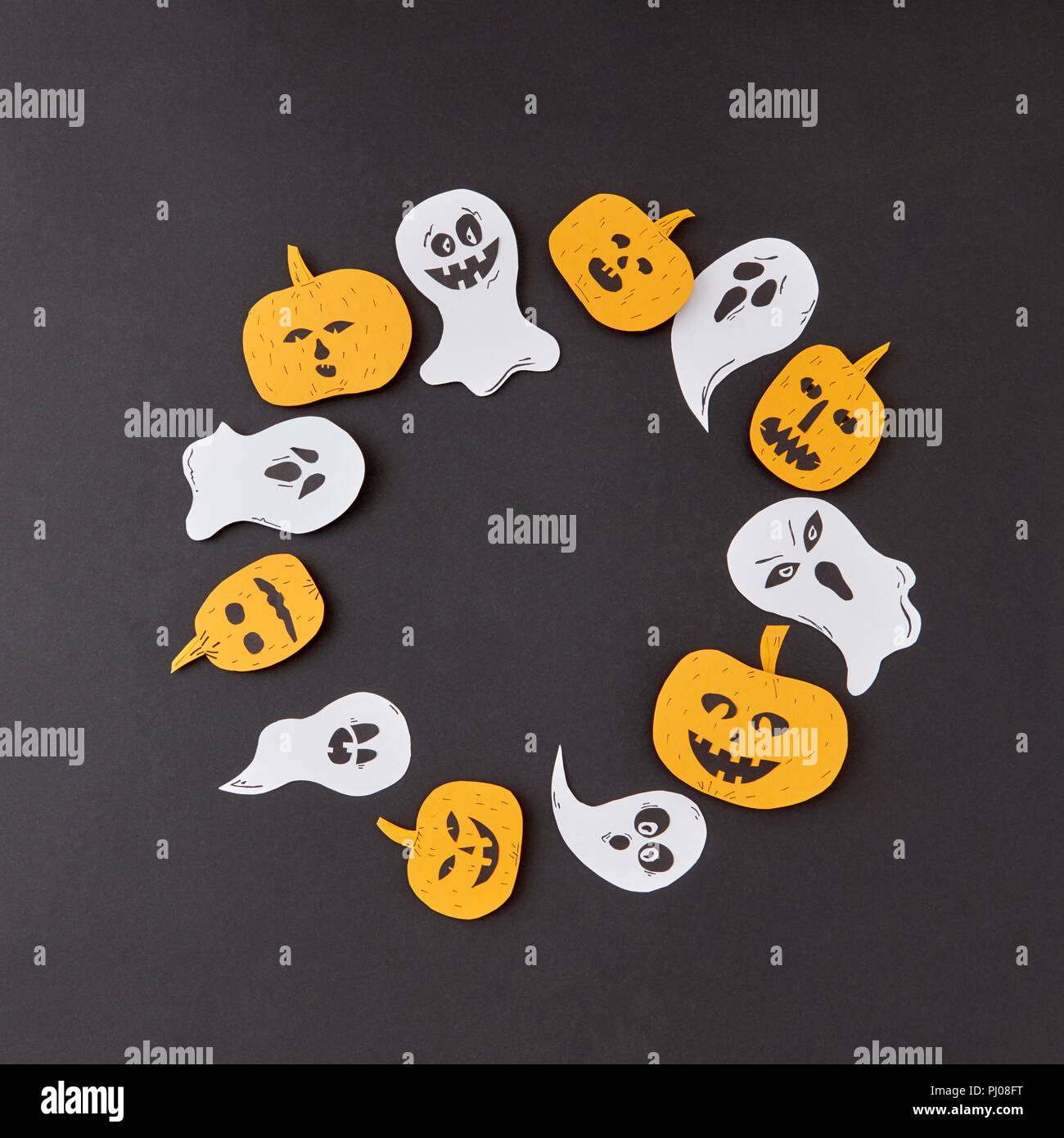 Cadre décoratif de round battant la main flottant esprit fantômes et citrouilles jaune souriant sur un fond de papier noir. Banque D'Images