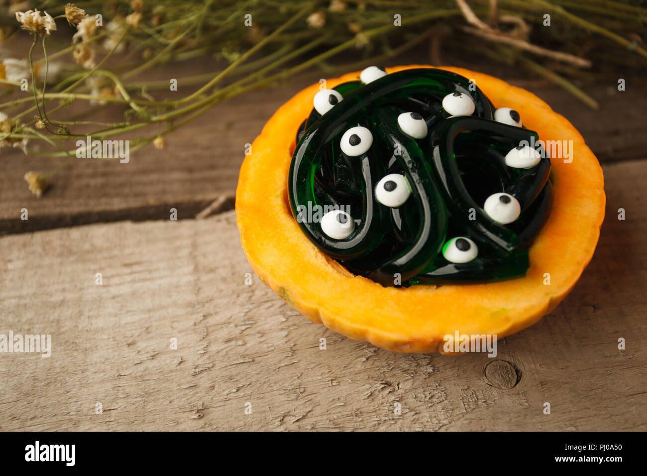 Halloween, la malbouffe et la confiserie concept - vert et noir les vers et les bonbons gommeux multicolores avec les yeux sur la table en bois, décoration de citrouille Banque D'Images
