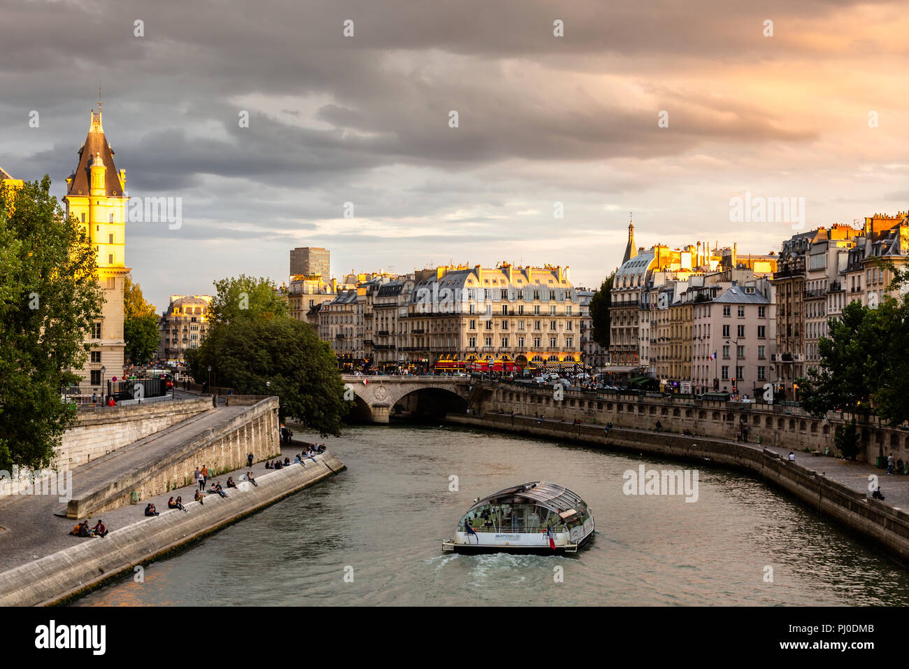 Bateau bus circulant le long de la seine dans la soirée, que les gens s'asseoir le long des rives de la rivière Banque D'Images