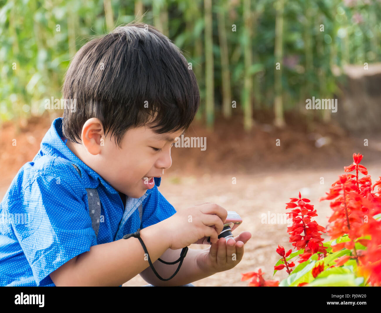 Petit garçon asiatique prendre caméra sur fleur de jardin, Banque D'Images