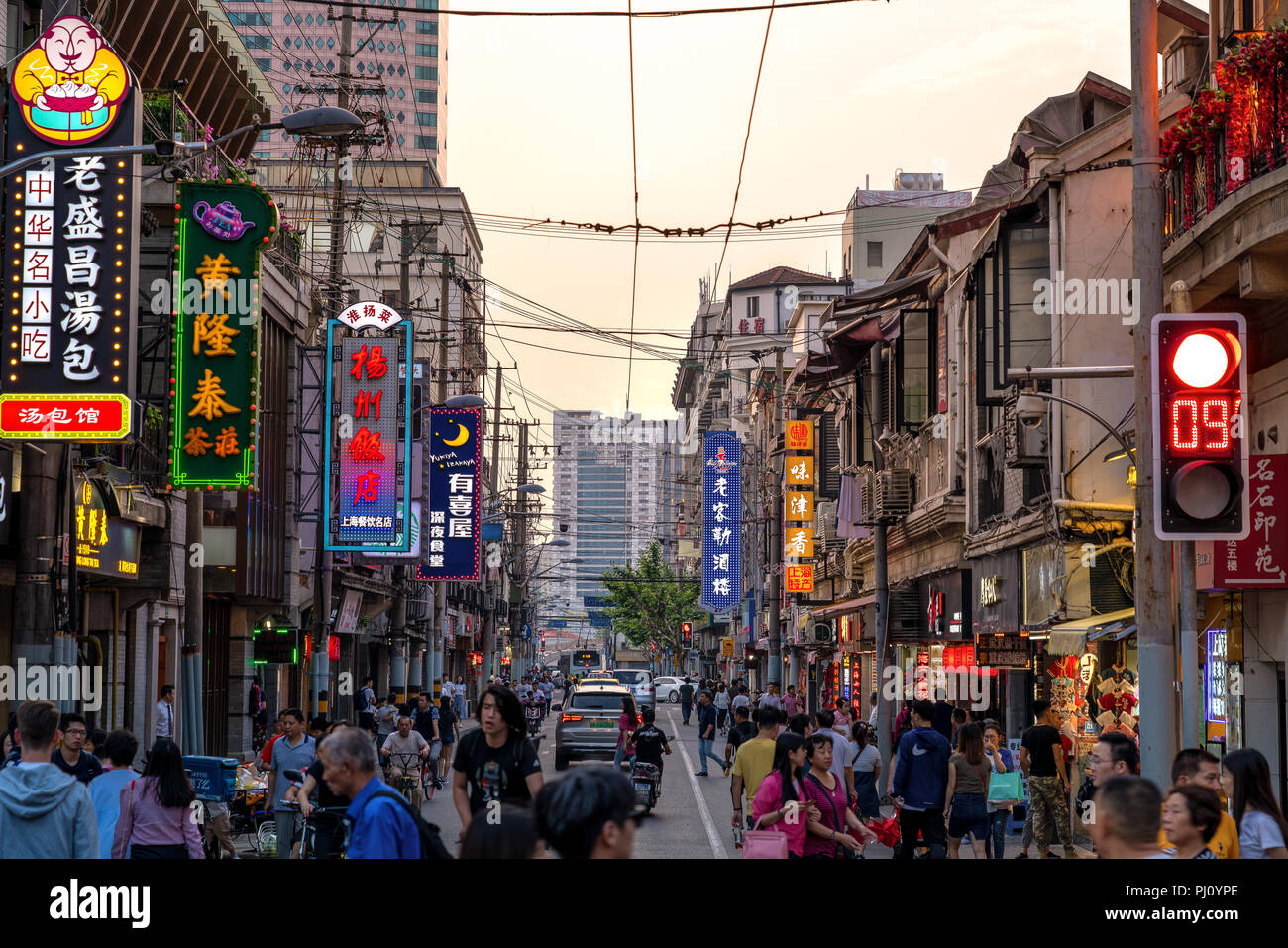 Foule de Chinois locaux déplacer rapidement le long d'une rue pleine de signes colorés à Shanghai, Chine, alors que le soleil se couche sur une journée d'été. Banque D'Images