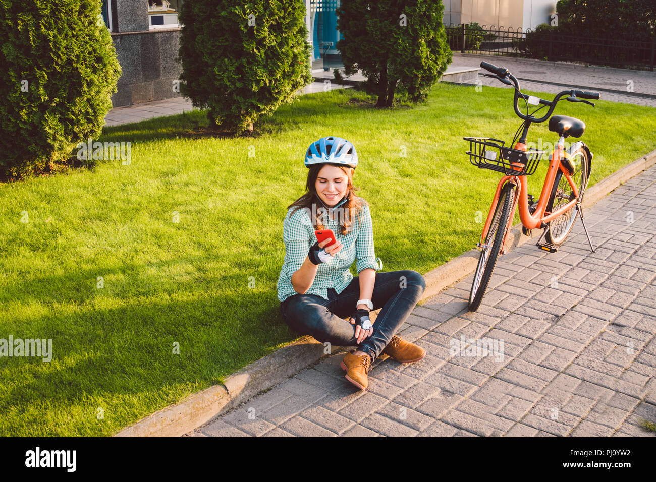 L'homme et de matériel roulant, vélo ville transports respectueux de l'environnement. Belle jeune femme de race blanche de repos assis sur l'herbe rouge utilise une mobil Banque D'Images