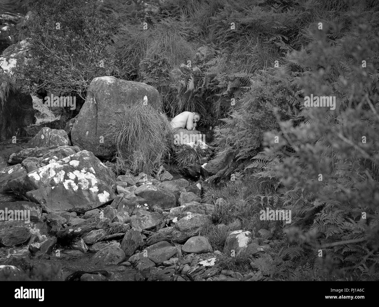 L'homme recroquevillé sur le sol dans un paysage rocheux, Irlande Banque D'Images