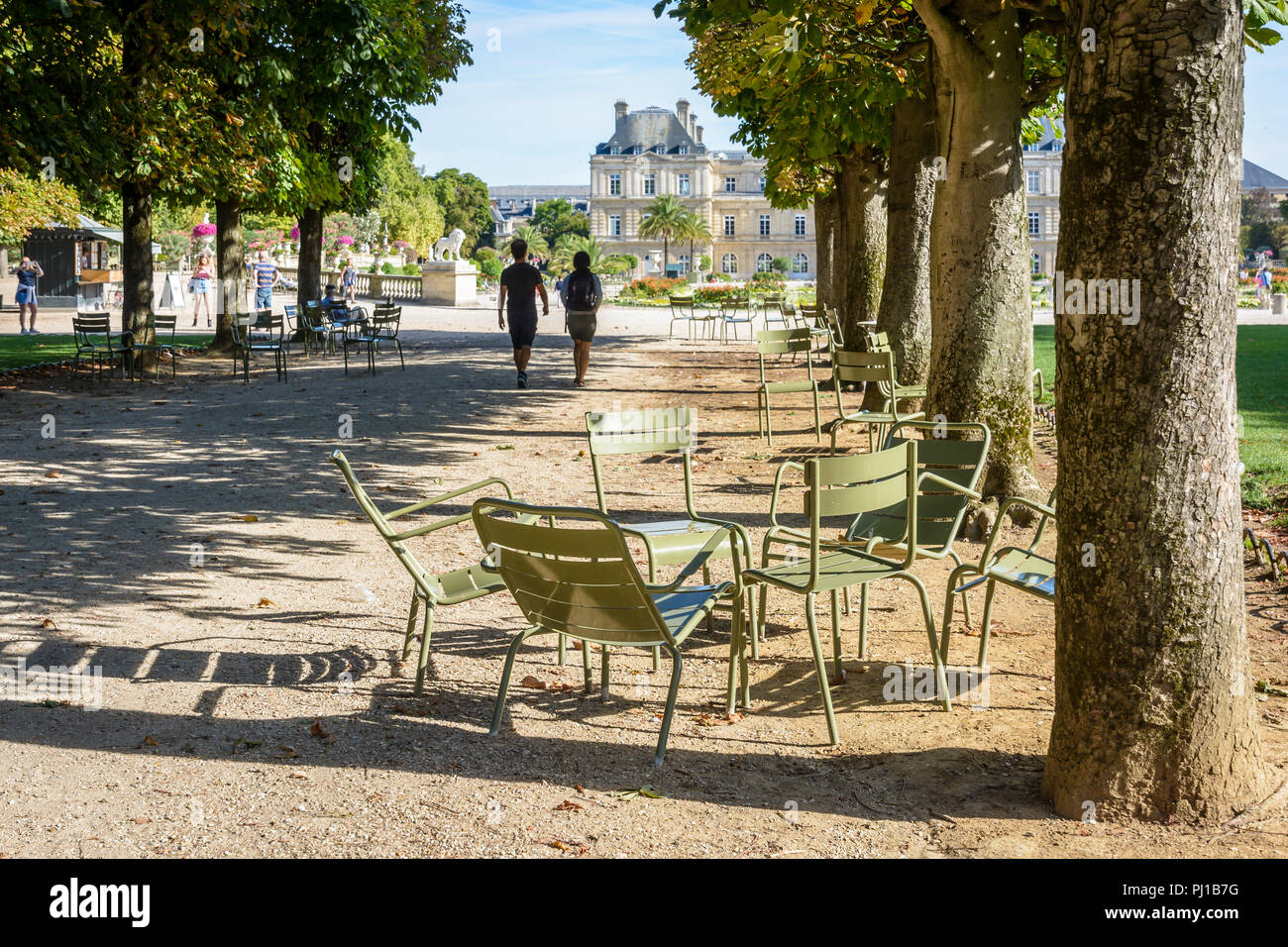 Les gens se promener ou se reposer sur des chaises dans le jardin du Luxembourg à Paris, France, par un matin ensoleillé avec le palais du Luxembourg dans l'arrière-plan. Banque D'Images