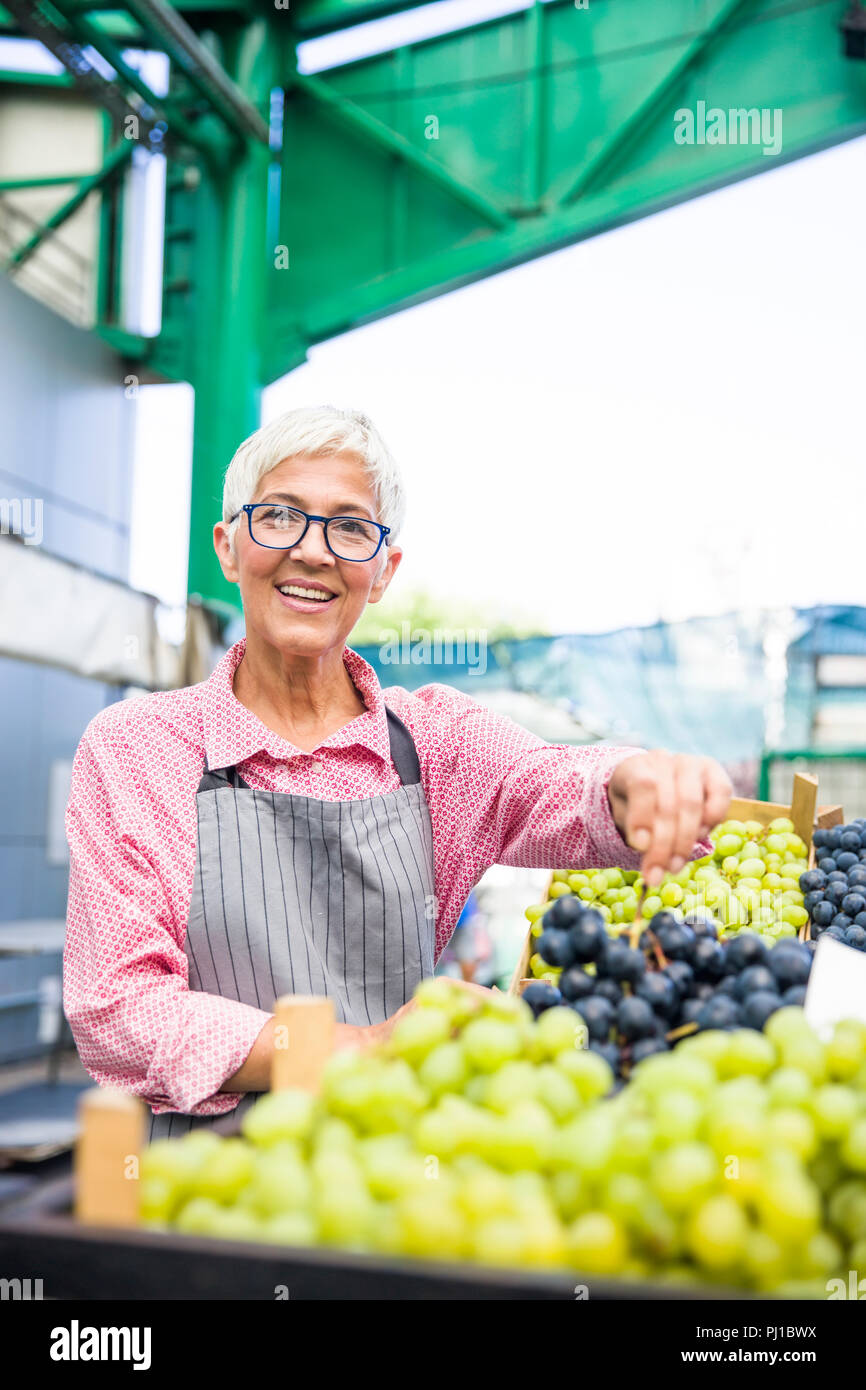 Portrait of senior woman vend des raisins sur market Banque D'Images