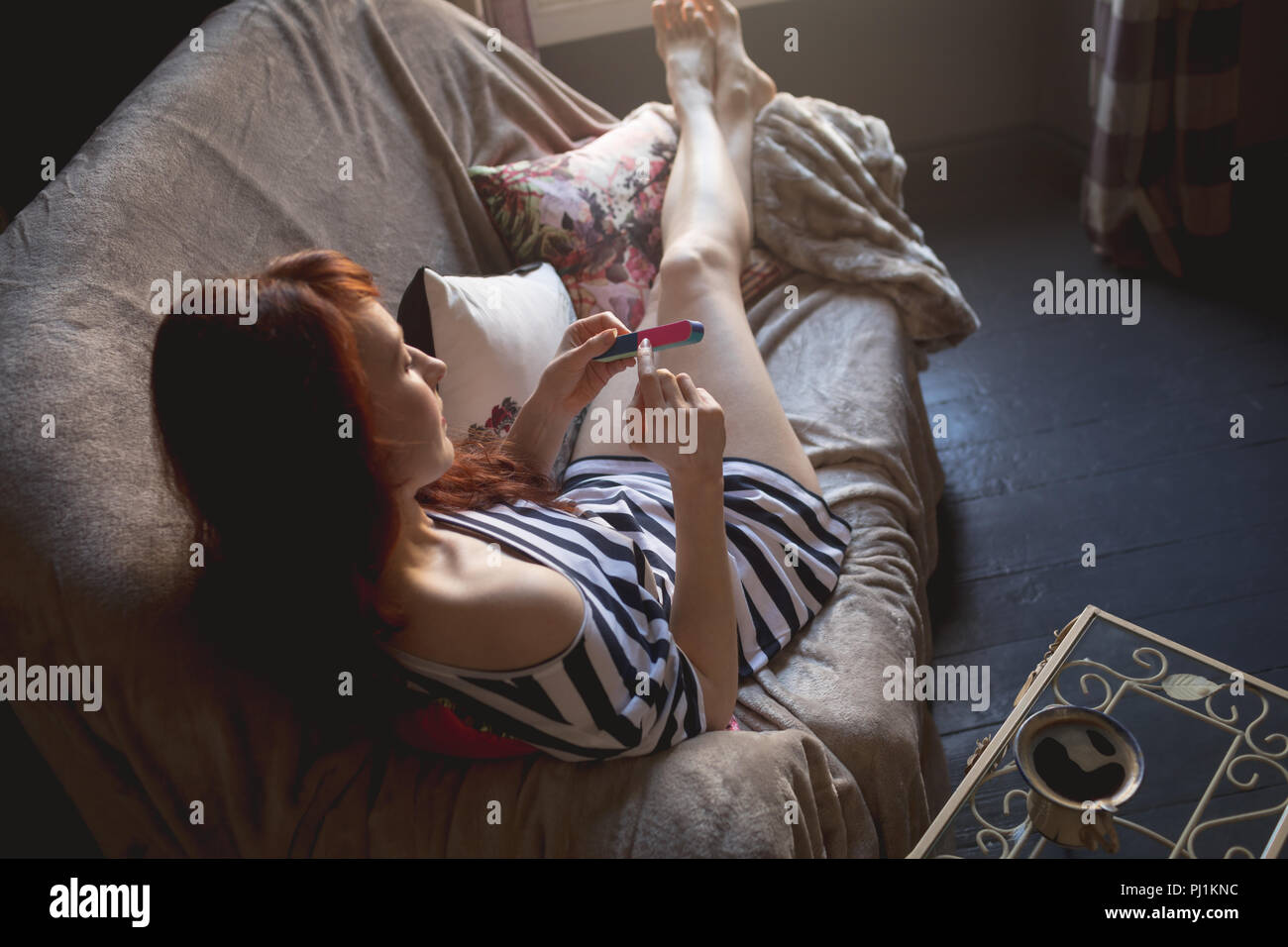 Femme à l'aide d'une lime à ongles sur canapé Banque D'Images