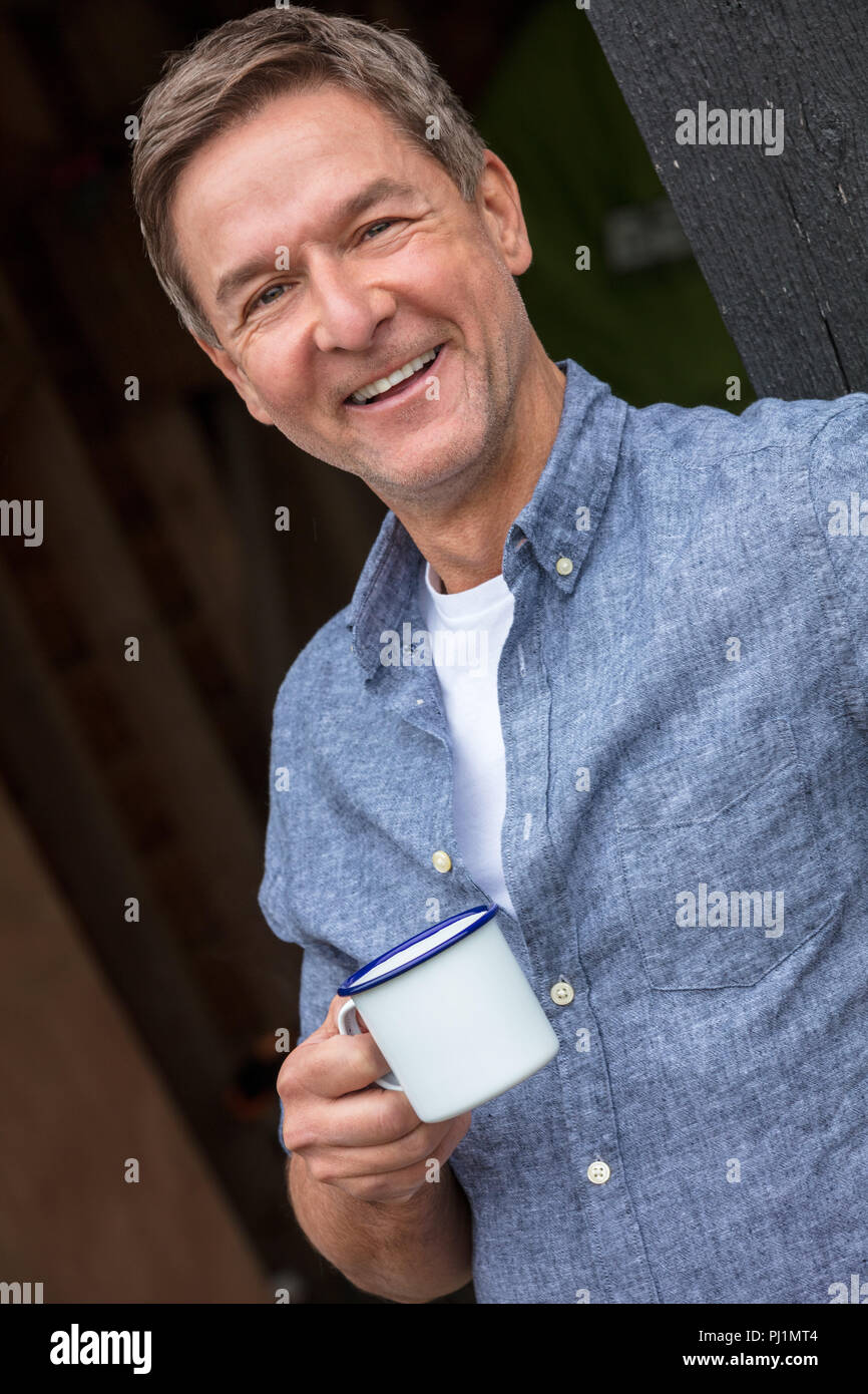 Portrait d'une belle réussite et heureux homme homme d'âge moyen portant une chemise bleue de boire du thé ou du café à partir d'un gobelet en étain Banque D'Images