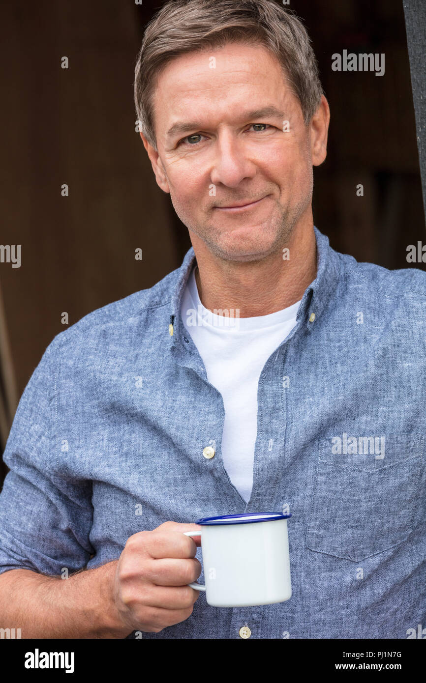 Portrait d'une belle réussite et heureux homme homme d'âge moyen portant une chemise bleue de boire du thé ou du café à partir d'un gobelet en étain Banque D'Images