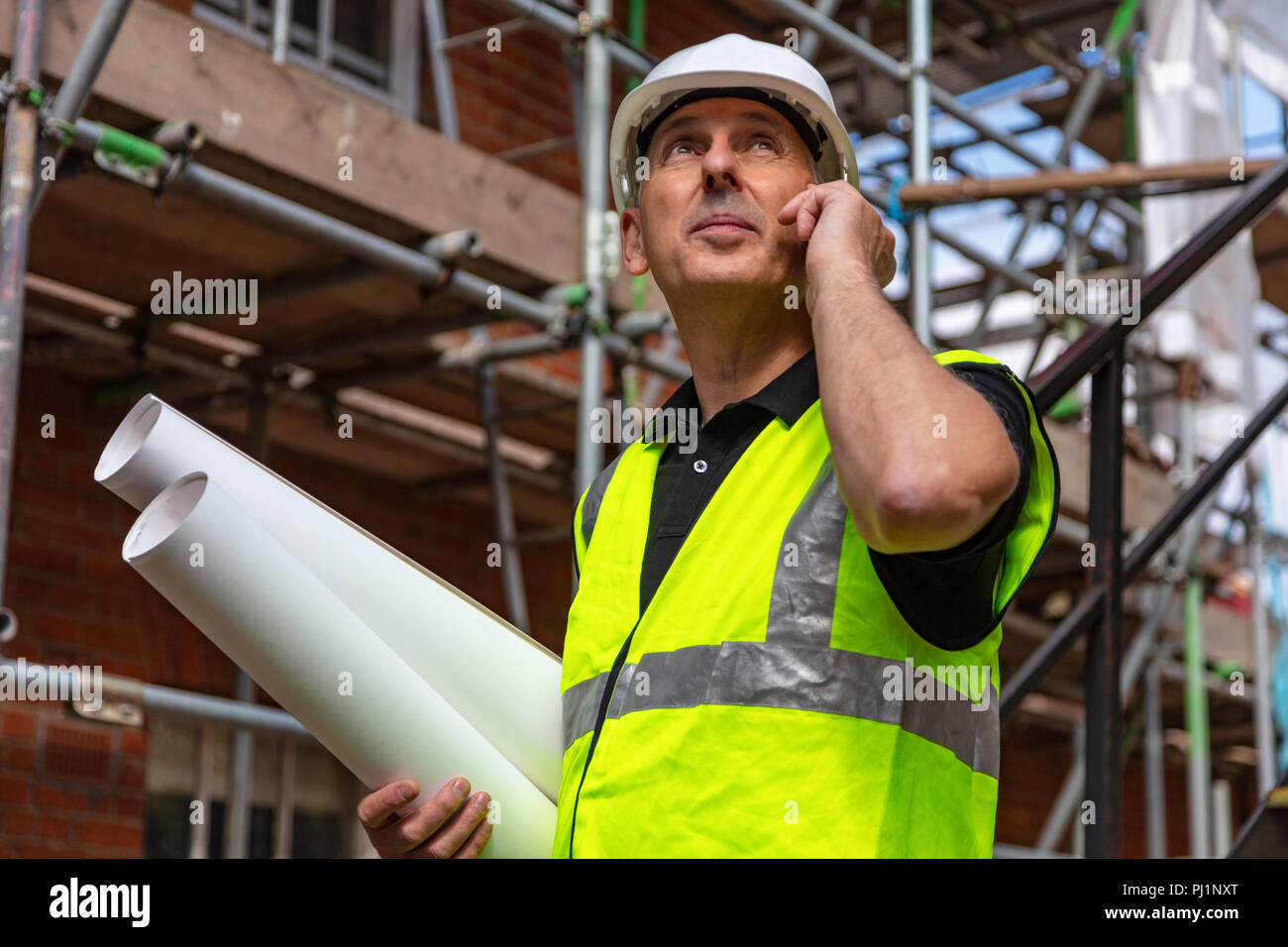 Homme builder contremaître, architecte ou travailleur on construction site holding building plans et de parler sur son téléphone cellulaire Banque D'Images