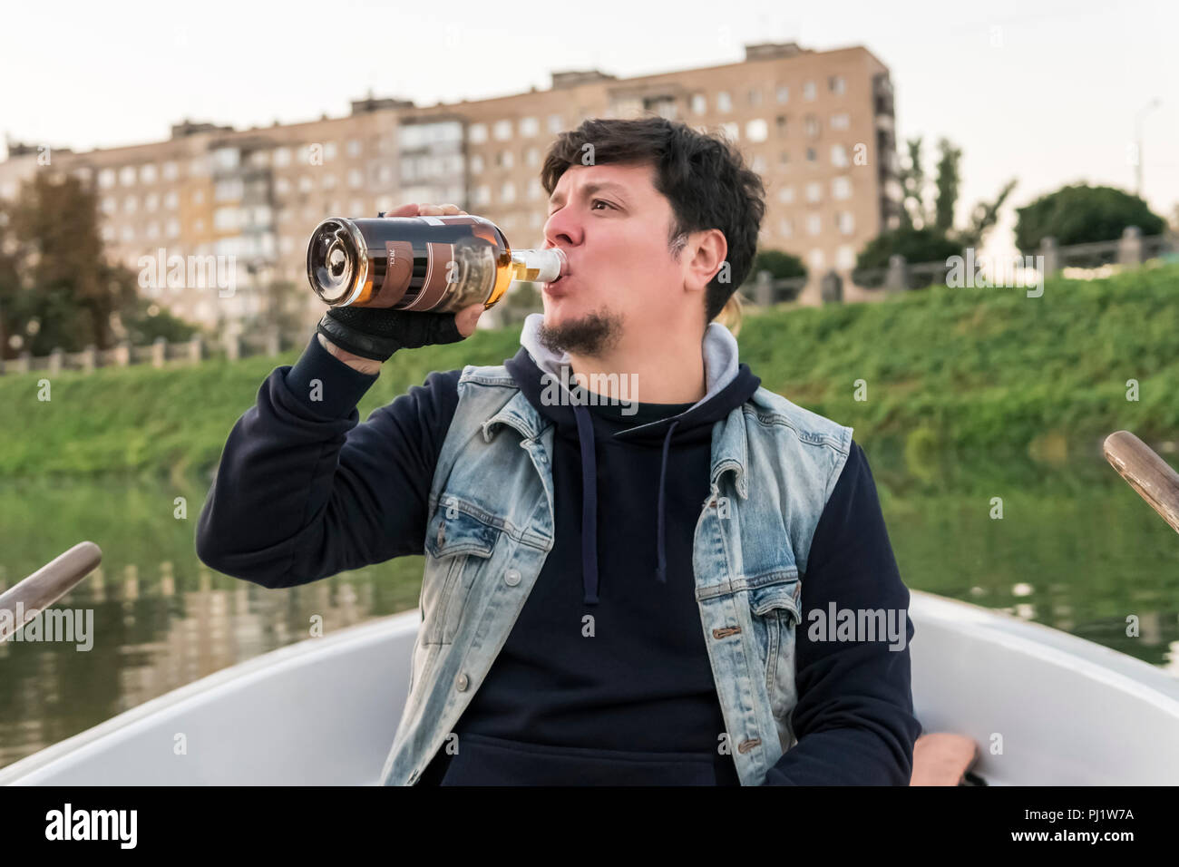 Homme barbu assis sur un bateau à boire du rhum d'une bouteille Banque D'Images