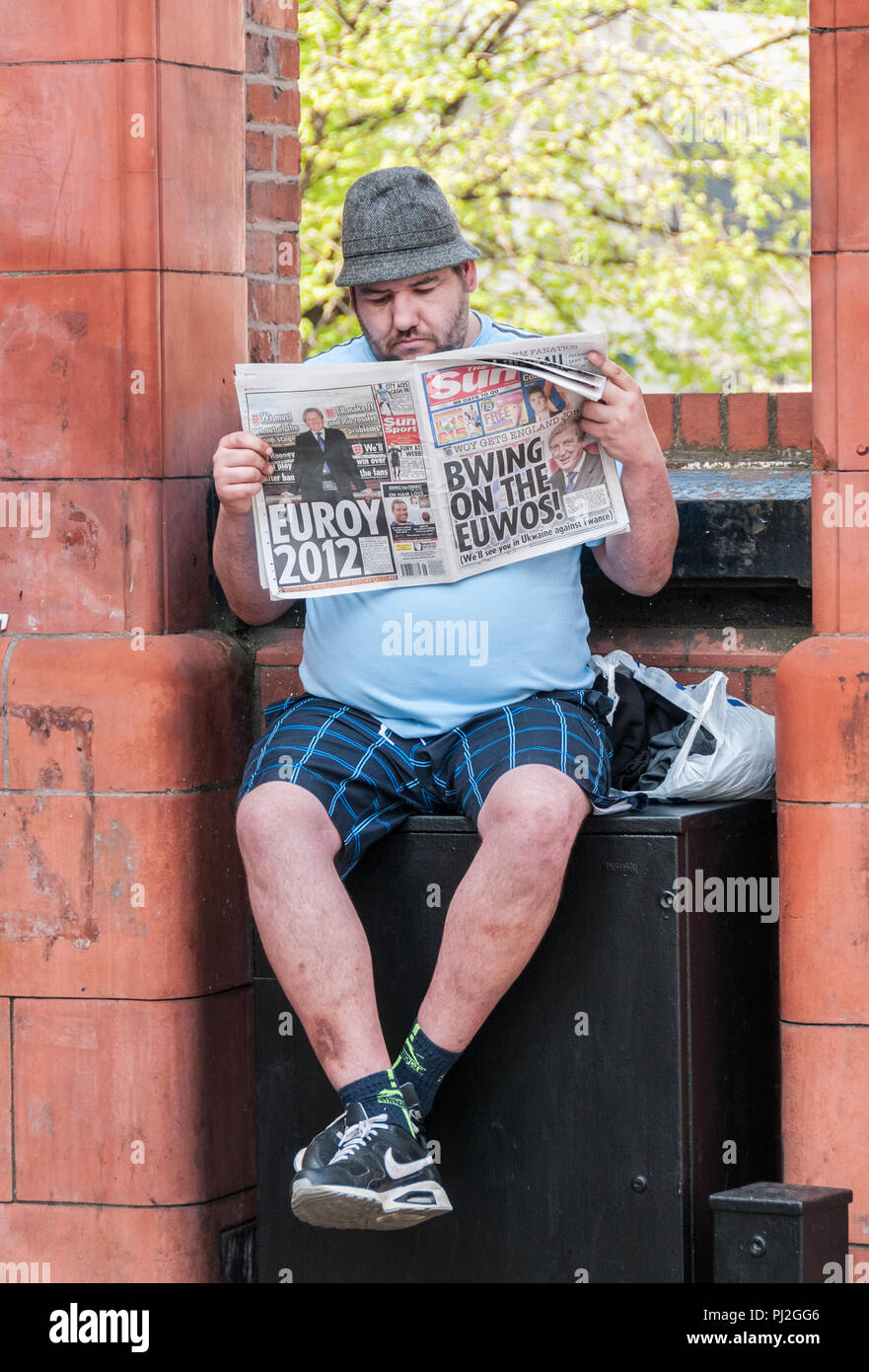 Homme portant un chapeau trilby, short et siégé au mur dans la lecture du journal Le Soleil de Manchester à partir de 2012 avant de l'euro tournoi de football Banque D'Images