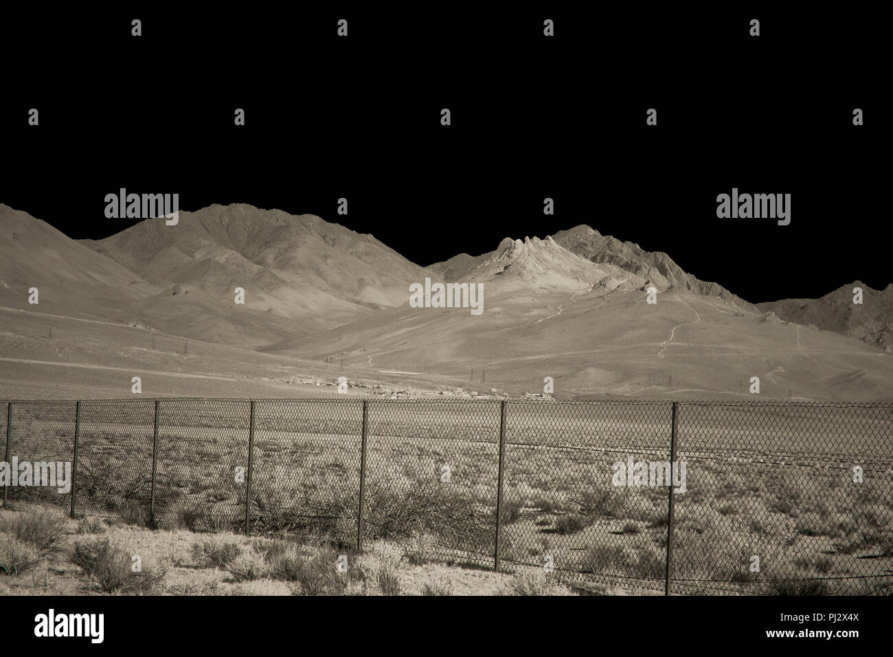 Une clôture divisant un côté du désert de l'autre de hautes montagnes dans l'arrière-plan sous un ciel noir. Banque D'Images