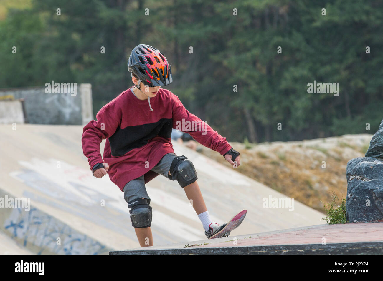 Young, 12 ans, beau garçon, le port d'équipement de planche à roulettes et la planche à roulettes. Casque coloré, genouillères, coudières, shorts, modèle Publié Banque D'Images