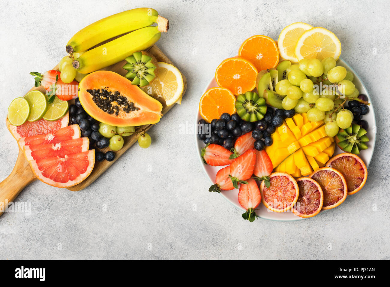 Fruits et baies sains en couleurs arc-en-ciel sur une assiette blanche et bois, fraises, mangue, raisins, bananes, pamplemousses sur la table gris clair, copy space, vue du dessus, selective focus Banque D'Images